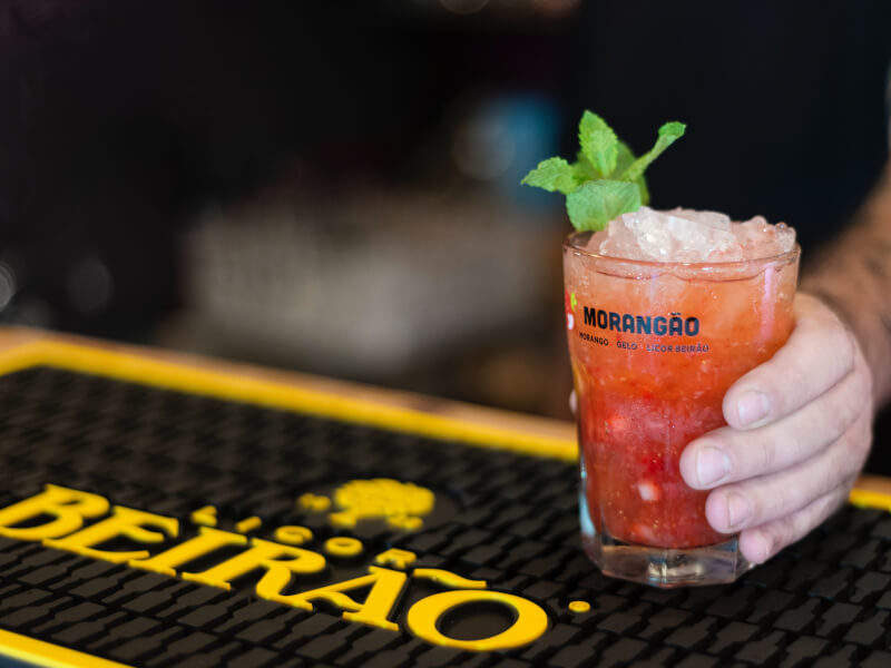 A bartender holds out a red coloured cocktail.